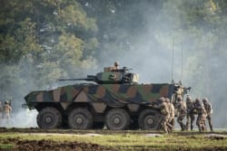 Des militaires en uniforme progressent en se protégeant auprès d'un VBCI