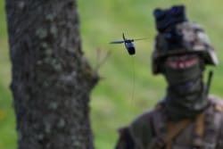 Un soldat en uniforme militaire observe un drone qui vole près d'un arbre.