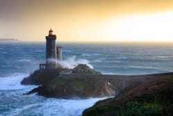 Phare au bord de la mer avec des vagues déferlantes, illuminé par un ciel doré au coucher du soleil. © Jérôme Houyvet