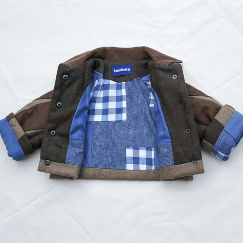 Gilet sans manches en denim bleu, suspendu à des cintres en bois sur un fond blanc.