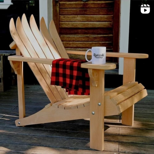 Une chaise en bois de style Adirondack avec une tasse sur l'accoudoir et un plaid en tartan rouge et noir drapé sur l'assise.
