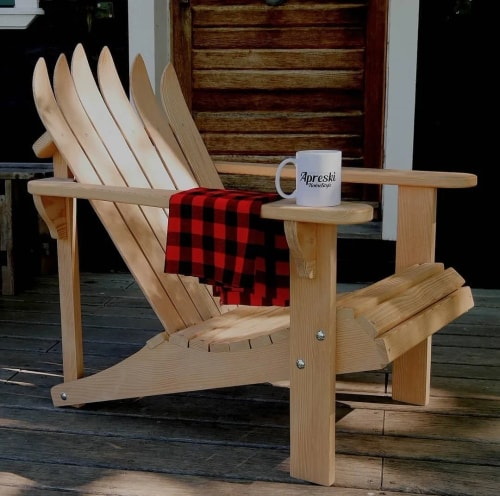 Chaise Adirondack en bois avec une couverture à carreaux rouge et noir drapée sur un bras et une tasse blanche avec l'inscription "Apreski Homestyle" posée sur le côté.