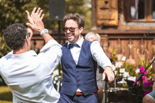 Un homme avec une barbe et un chapeau travaille sur un fauteuil en bois dans un atelier encombré d'outils et de matériaux. La lumière naturelle entre par la fenêtre, créant une ambiance chaleureuse et artisanale.