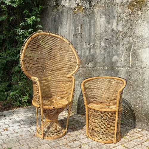 Deux chaises en osier, une grande chaise avec un dos haut et une petite chaise, devant un mur en béton mossu.