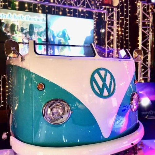 Image d'un véhicule bar Volkswagen vintage en bleu et blanc, décoré avec des lumières brillantes en arrière-plan.