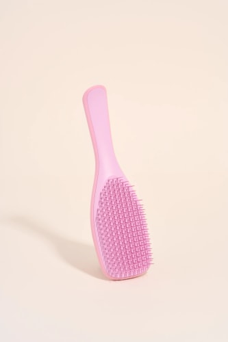 Une brosse à cheveux rose sur un fond neutre.