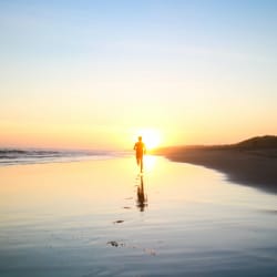 Une personne court seule sur une plage au lever du soleil, laissant des empreintes de pas derrière elle sur le sable mouillé.