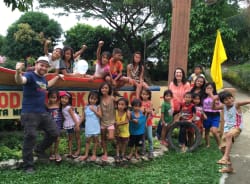 Un homme et une femme posent avec un grand groupe d'enfants souriants devant une enseigne en bois dans un parc verdoyant.
