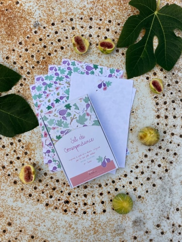 Invitation décorée de motifs floraux, posée sur une table mouchetée, entourée de feuilles vertes et de noisettes.