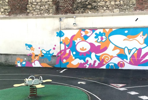 Une peinture murale colorée sur le thème de l'océan, avec des poissons et des formes abstraites, située dans une cour de récréation avec un jeu à ressort au premier plan.