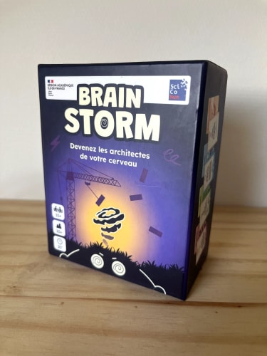 Boîte de jeu de société « Brain Storm » posée sur une table en bois, avec un cerveau, des éclairs et des éléments colorés sur la couverture.