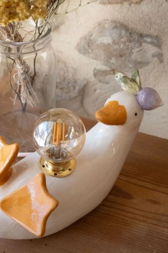 Trois bougies en céramique colorée disposées en triangle, ornées de médaillons gravés représentant une maison étoilée, un oiseau avec des fleurs et un motif botanique. Fond en bois clair.