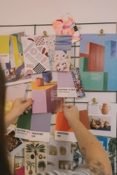 Une main tient plusieurs feuilles de papier imprimées avec des motifs colorés abstraits, floraux et géométriques sur une table blanche.