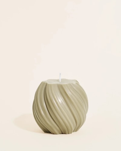 Bougie blanche Piana à surface texturée en forme de tourbillon posée sur un miroir rond, avec un flacon en verre ambré contenant des bâtonnets parfumés en arrière-plan sur une surface beige.