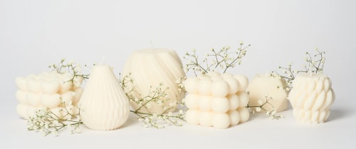 Bougies blanches de la marque Flamme de différentes formes décorées avec des petites fleurs blanches sur fond clair.