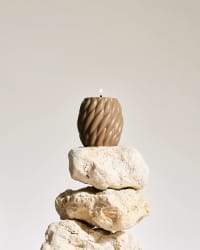 Bougie cube orange Fiamme composée de petites sphères, posée sur un miroir rond, avec un diffuseur d'arômes en verre brun et des bâtonnets en arrière-plan, le tout sur une surface claire.