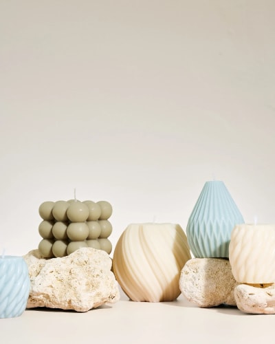 Trois bougies blanches Fiamme de formes différentes placées sur une tranche de bois, avec un fond gris neutre.