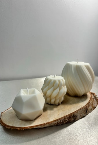 Trois bougies Fiamme blanches de formes différentes posées sur une tranche de bois : une bougie géométrique, une bougie torsadée, et une bougie à contours ondulés.