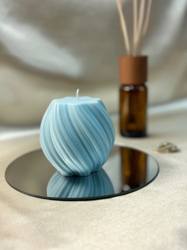 Bougie bleue Fiamme à motifs torsadés posée sur un miroir circulaire, avec un diffuseur d'arômes en arrière-plan sur une surface beige.
