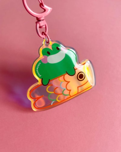 Un suncatcher sticker d'une illustration colorée représentant un parc avec un pédalo en forme de canard, une grenouille et un cochon dedans, des fleurs souriantes devant et des arbres derrière sur un fond vert.