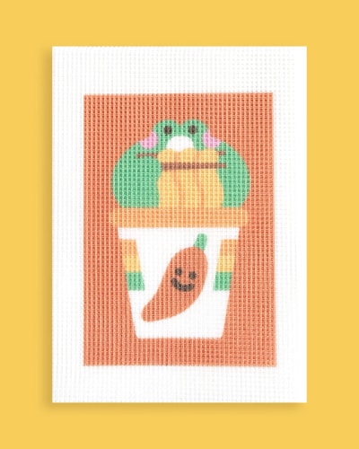 Une illustration sur un canevas à broder d'un ours brun tenant une glace un dango de couleur rose, blanc et vert