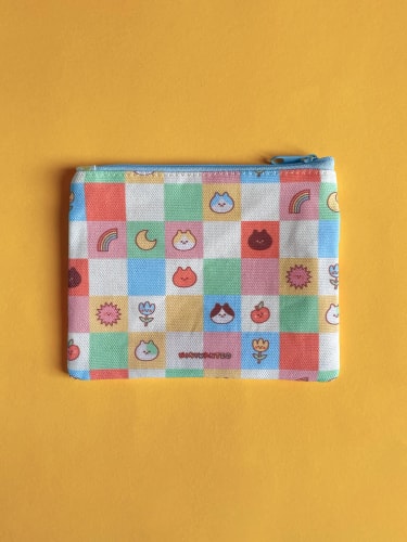 Une pochette en tissu coloré avec des motifs d'icônes de voyage au Japon, tenu par une main, sur un fond jaune.