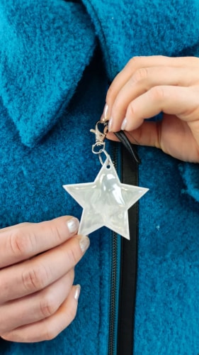 Gros plan d'un enfant portant une veste rose avec un réflecteur en forme de cœur accroché à la fermeture éclair. L'enfant s'appuie sur la main de son parent, l'atmosphère de l'image est chaleureuse et bienveillante.