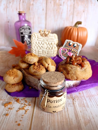 Une composition de pâtisseries artisanales, tablettes de chocolat décorées, dés de jeu de rôle mauves et enveloppes kraft sur une surface claire, agrémentée de fleurs séchées.