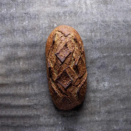 Une miche de pain artisanal brun avec une croûte gravée en motifs géométriques, posée sur une surface grise rugueuse.