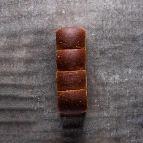 Quatre pains bruns carrés alignés verticalement sur une surface grise texturée.