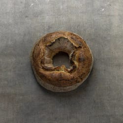 Pain rond avec un trou au centre, coloration et texture croustillante, posé sur une surface grise
