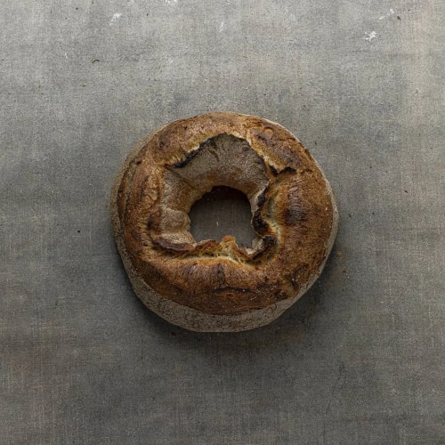 Pain rond avec un trou au centre, coloration et texture croustillante, posé sur une surface grise