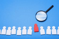 Une loupe agrandissant une figure humaine rouge parmi des silhouettes blanches sur un fond bleu, pour illustrer les services de recrutement de Keystone Recrutement
