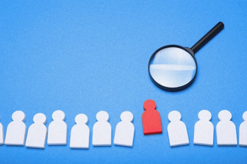 Une loupe agrandissant une figure humaine rouge parmi des silhouettes blanches sur un fond bleu, pour illustrer les services de recrutement de Keystone Recrutement