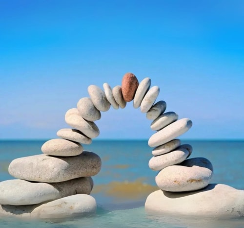 Un arc de pierres soigneusement empilées au bord de l'eau, avec un ciel bleu en arrière-plan, pour illustrer le soutien de Keystone dans votre processus de recrutement.