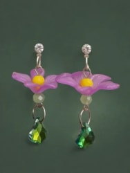 Paire de boucles d'oreilles pendantes avec une fleur violette à cœur jaune, une perle claire et une pampille en cristal vert, sur fond vert foncé.