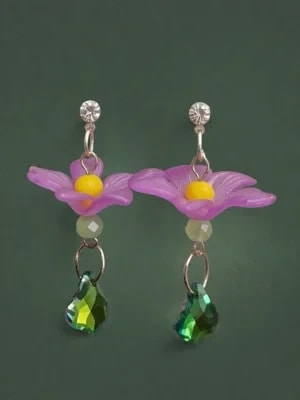 Paire de boucles d'oreilles pendantes avec une fleur violette à cœur jaune, une perle claire et une pampille en cristal vert, sur fond vert foncé.