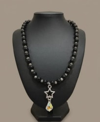 Collier composé de perles noires et argentées, porté par un buste de présentation, avec un pendentif en forme d'étoile argentée surmontant une breloque en cristal brillant.
