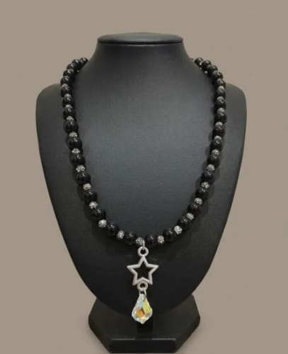 Collier composé de perles noires et argentées, porté par un buste de présentation, avec un pendentif en forme d'étoile argentée surmontant une breloque en cristal brillant.